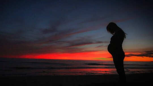 a pregnant woman in silhouette with the sunrise in the background